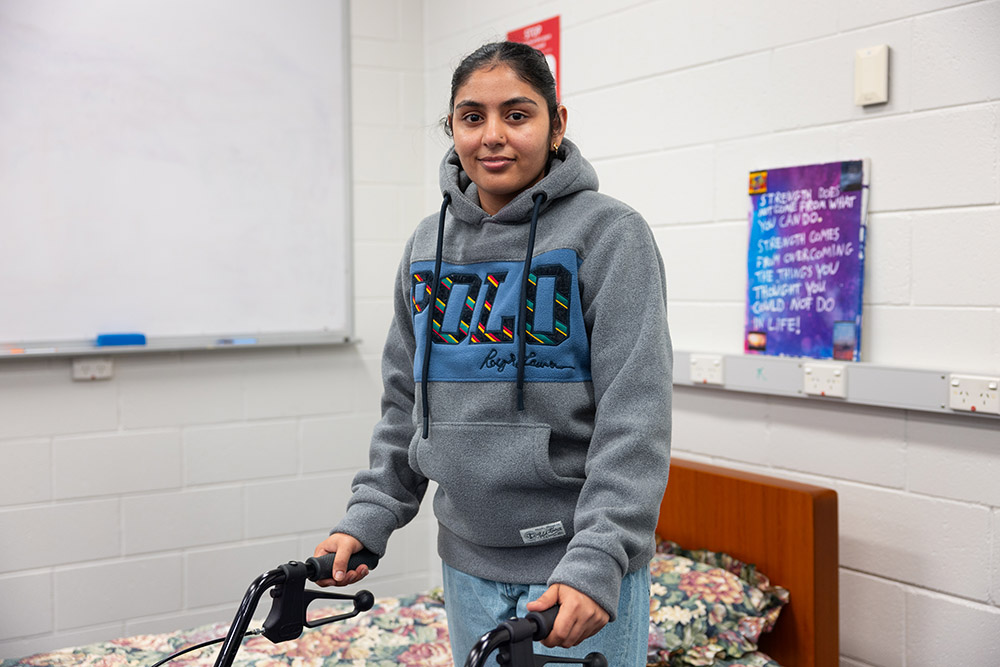 Female Allied Health student learning hands-on, operating an assistive mobility walker.